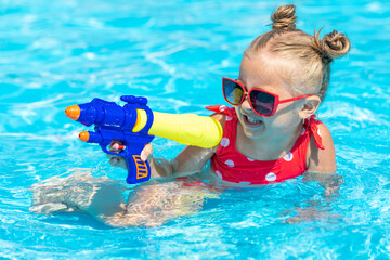 Laughing child playing with water gun in outdoor swimming pool on summer day. Pool toys and water...