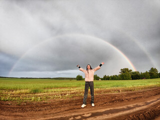 An adult girl in a field with a stormy sky with clouds and grey rainbow. A woman having fun outdoors on rural and rustic nature. The Grey Rainbow and the Ban on LGBT symbols in Russia
