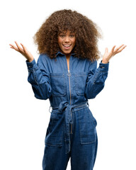 African american woman wearing blue jumpsuit happy and surprised cheering expressing wow gesture