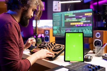 Composer creating soundtracks on stereo gear and greenscreen display on mobile device, mixing and...