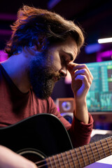 Stressed sleepy artist practicing acoustic instrument in his home studio, recording new tunes and...
