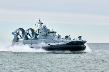 Hovercraft warship armed with armament sails into sea toward military target to attack and destroy enemy, military hovercraft ship performing strategic maneuver, Russian sea power deployment - obrazy, fototapety, plakaty