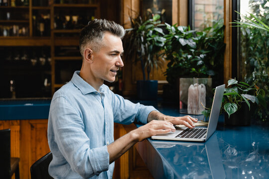 Concentrated successful caucasian mature businessman CEO freelancer working remotely on laptop, e-banking, doing online shopping, watching webinars, e-learning in cafe restaurant