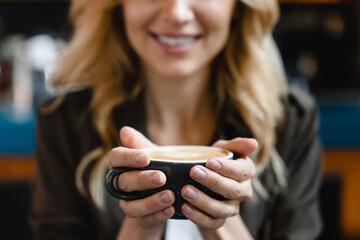 Fototapeta premium Focused shot. Young caucasian beautiful woman holding cup mug of hot beverage coffee tea enjoying aroma while having breakfast brunch in cafe restaurant