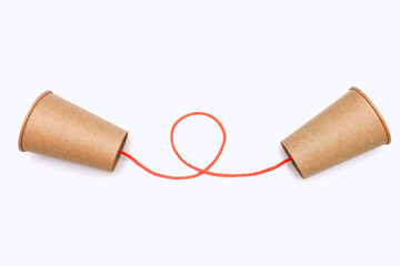 Two paper cups united by an orange thread isolated on a white background close-up. Cardboard kraft...