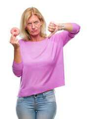 Middle age blonde woman eating pink donut over isolated background with angry face, negative sign showing dislike with thumbs down, rejection concept