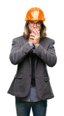 Young handsome architec man with long hair wearing safety helmet over isolated background shocked covering mouth with hands for mistake. Secret concept.