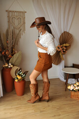 jovem mulher estilo vaqueira com bota cowtry, ambiente interior estilo boho tons marrons