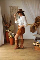 jovem mulher estilo vaqueira com bota cowtry, ambiente interior estilo boho tons marrons