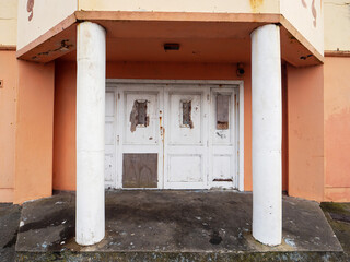 Old worn out entrance to abandoned home or hotel with white color doors, columns and orange color...