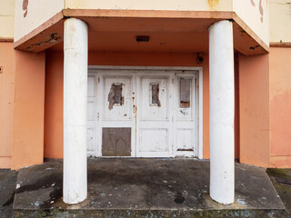 Old worn out entrance to abandoned home or hotel with white color doors, columns and orange color walls. Recession and business shot down concept.
