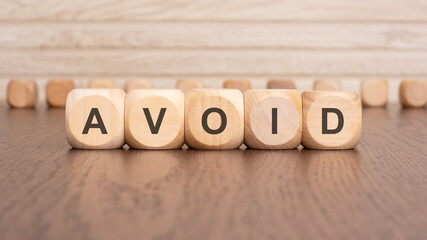 the text 'AVOID' is written on wooden cubes on a brown background