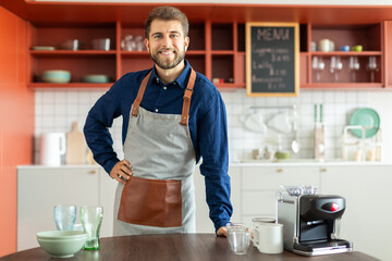 Portrait of handsome male cafe owner standing indoors, looking at camera and smiling, free space