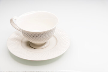 Uma xícara branca de porcelana amarelada em um pires sobre um fundo branco. Xícara vazia, fundo neutro. tons neutros. Café, chá, bebidas quentes. Requinte.