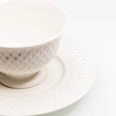 Uma xícara branca de porcelana amarelada em um pires sobre um fundo branco. Xícara vazia, fundo neutro. tons neutros. Café, chá, bebidas quentes. Requinte.
