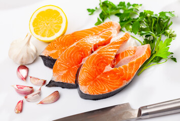 Fresh uncooked salmon fish with greens and lemon on a ceramic plate with kitchen knife