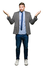 Handsome business man wearing suit and tie clueless and confused expression with arms and hands raised. Doubt concept.