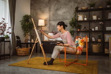 one woman female artist paint canvas on easel hold paintbrush at home