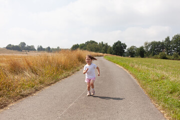 Little girl happily running along a quiet rural road, surrounded by the beauty and tranquility of the countryside