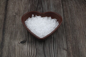 Fototapeta na wymiar Sea salt in heart shaped bowl on black stone table