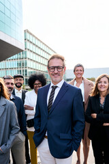 Vertical cheerful smiling team of diverse business people in formal suit looking confident camera with positive faces gathered outside the work building. Happy corporate work team posing for portrait