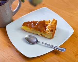 Piece of caramel apple pie served in a plate with a cup of coffee on the table