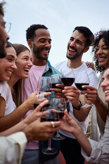 Vertical. Gathering of diverse cheerful friends toasting red wine and celebrating birthday party event outdoor. Young laughing people together enjoying free time on weekend