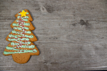 A delicious Christmas tree ginger bread with green icing, sprinkles and a yellow star on a wooden background