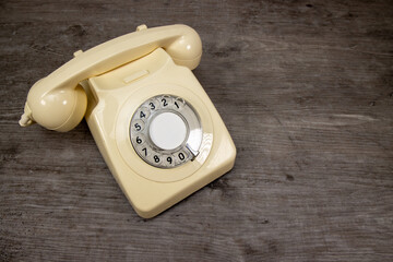 An old retro cream rotary telephone on a wooden background