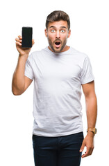 Young handsome man showing smartphone screen over isolated background scared in shock with a...