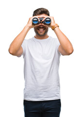 Young handsome man looking through binoculars over isolated background with a happy face standing...