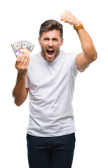 Young handsome man holding stack of dollars over isolated background annoyed and frustrated...