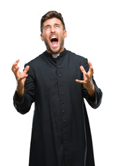 Young catholic christian priest man over isolated background crazy and mad shouting and yelling...