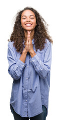Young hispanic business woman praying with hands together asking for forgiveness smiling confident.