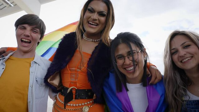 Low angle. A group of diverse happy young people are posing looking camera embracing with rainbow flags laughing and sharing the moments of fun LGBT event outdoor