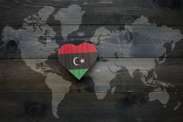 wooden heart with national flag of libya near world map on the wooden background.