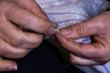Close-up view of woman's hands in sewing process. Sewing fabric by hand with needle at workplace....