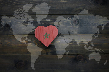 wooden heart with national flag of morocco near world map on the wooden background.