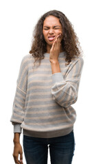 Beautiful young hispanic woman wearing stripes sweater touching mouth with hand with painful expression because of toothache or dental illness on teeth. Dentist concept.