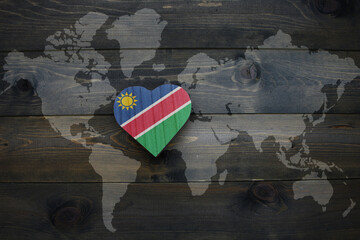 wooden heart with national flag of namibia near world map on the wooden background.