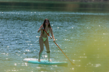 Latina Woman in Bikini Enjoying Paddleboarding on Lake with bushes obscuring the foreground