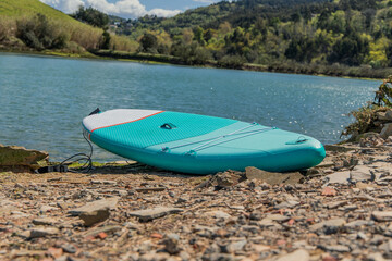 Blue Stand-Up Paddle surf board Resting on Riverbank in Summer