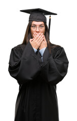 Young hispanic woman wearing graduated cap and uniform shocked covering mouth with hands for mistake. Secret concept.