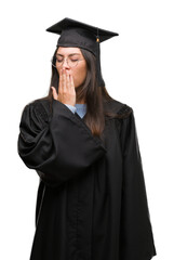 Young hispanic woman wearing graduated cap and uniform bored yawning tired covering mouth with...