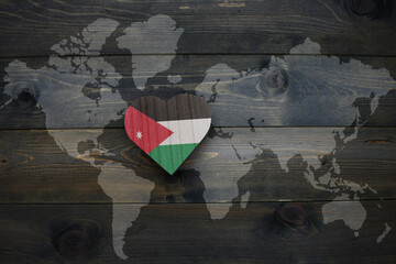 wooden heart with national flag of jordan near world map on the wooden background.