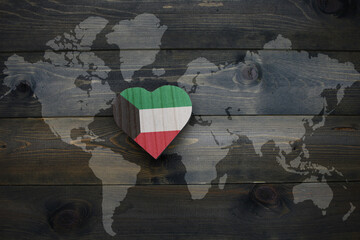 wooden heart with national flag of kuwait near world map on the wooden background.