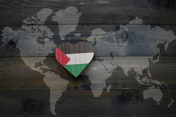 wooden heart with national flag of palestine near world map on the wooden background.