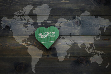 wooden heart with national flag of saudi arabia near world map on the wooden background.