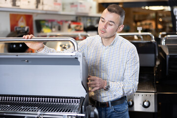 Young man buyer chooses bbq grill in hardware store