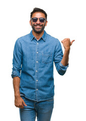 Adult hispanic man wearing sunglasses over isolated background smiling with happy face looking and pointing to the side with thumb up.